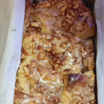 A delicious homemade cinnamon apple pull-apart bread in a parchment-lined loaf pan, drizzled with a sweet glaze and topped with crunchy apple bits.