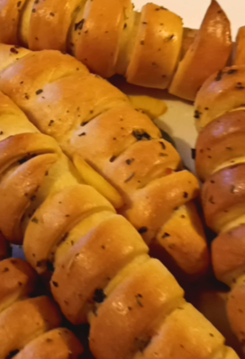 Golden-brown cheesy crescent rolls with a glossy buttery finish, arranged on a plate. The warm lighting enhances their inviting, fluffy texture.