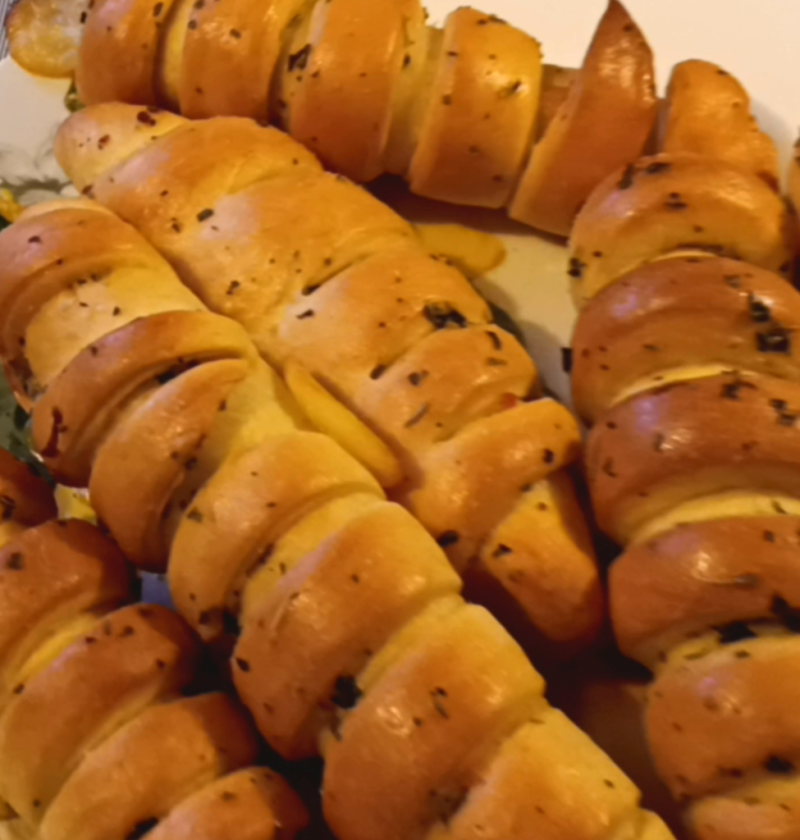 Golden-brown cheesy crescent rolls with a glossy buttery finish, arranged on a plate. The warm lighting enhances their inviting, fluffy texture.