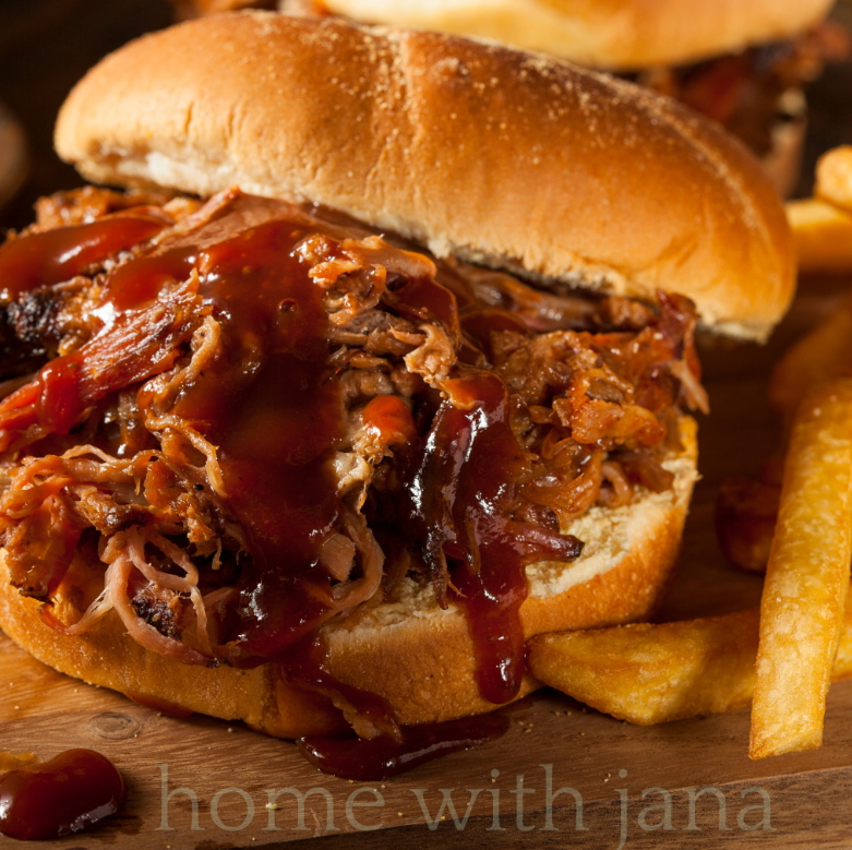 Slow-cooked pulled pork sandwich piled high on a soft sandwich bun and topped with rich barbecue sauce. The tender shredded pork is juicy and caramelized, served with crispy fries on a rustic wooden board in warm cozy lighting.