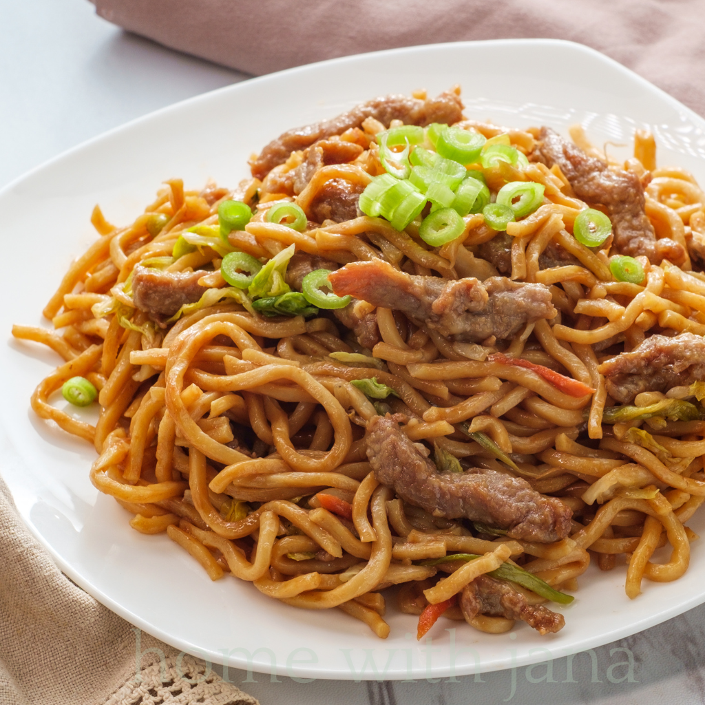 A beautifully plated bowl of side dish lo mein noodles with a glossy savory sauce topped with crisp vegetables.