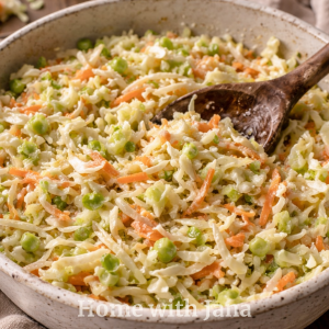 Creamy Southern-style coleslaw with crisp shredded cabbage, carrots, and red onion, served in a rustic ceramic bowl and garnished with fresh parsley in a cozy kitchen setting.