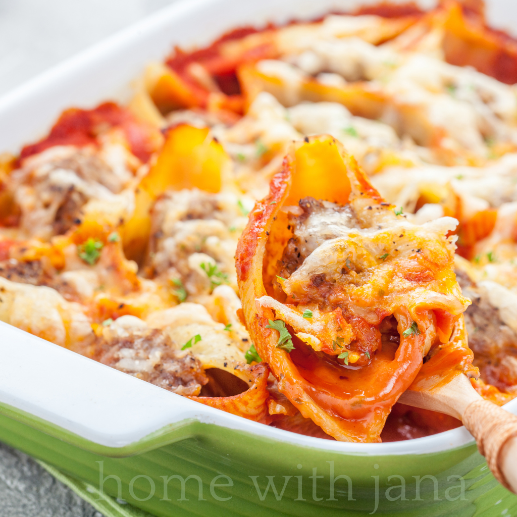Freshly baked stuffed pasta shells in a green casserole dish topped with melted cheese and marinara, set in a cozy rustic kitchen with warm lighting