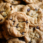 Close-up of golden brown chocolate chip cookies with crisp edges and soft centers, stacked and overlapping for a cozy homemade feel