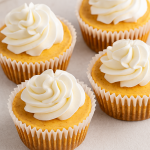 A high-resolution image showing four no-bake pumpkin cheesecake cups in clear glass containers, each layered with a graham cracker crust, smooth pumpkin cheesecake filling, and topped with whipped cream.