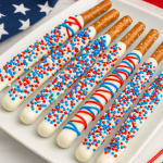 Patriotic-themed dessert tray with white chocolate dipped pretzel rods decorated in red, white, and blue sprinkles