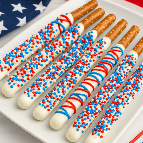 Patriotic-themed dessert tray with white chocolate dipped pretzel rods decorated in red, white, and blue sprinkles