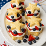 Star-shaped shortcakes layered with whipped cream, strawberries, and blueberries on a white serving tray with patriotic accents