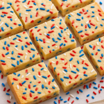 A batch of patriotic-themed firecracker cookie bars with red, white, and blue sprinkles, sliced into squares and arranged on a baking tray