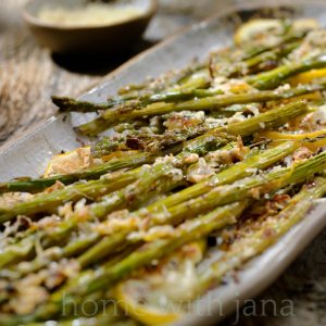 Sheet pan of roasted asparagus topped with melted Parmesan cheese and lemon slices