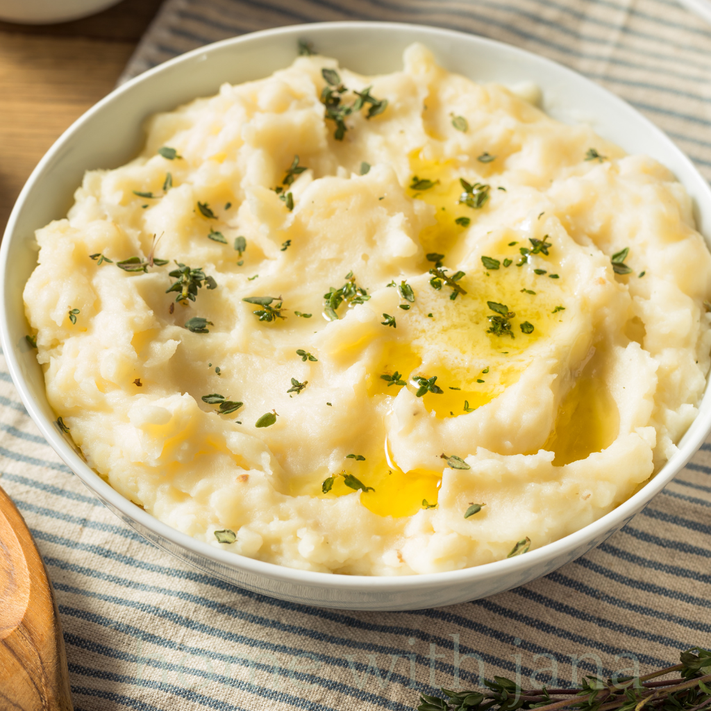Bowl of creamy mashed potatoes topped with melted butter and fresh herbs