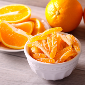 Bowl of homemade candied orange peel coated in sugar with fresh oranges in the background