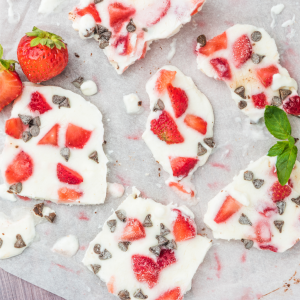 Frozen yogurt bark topped with fresh strawberries and chocolate chips on parchment paper