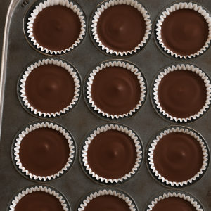 Homemade peanut butter cups with glossy chocolate tops and creamy centers, set in white muffin liners and chilled in a muffin tin