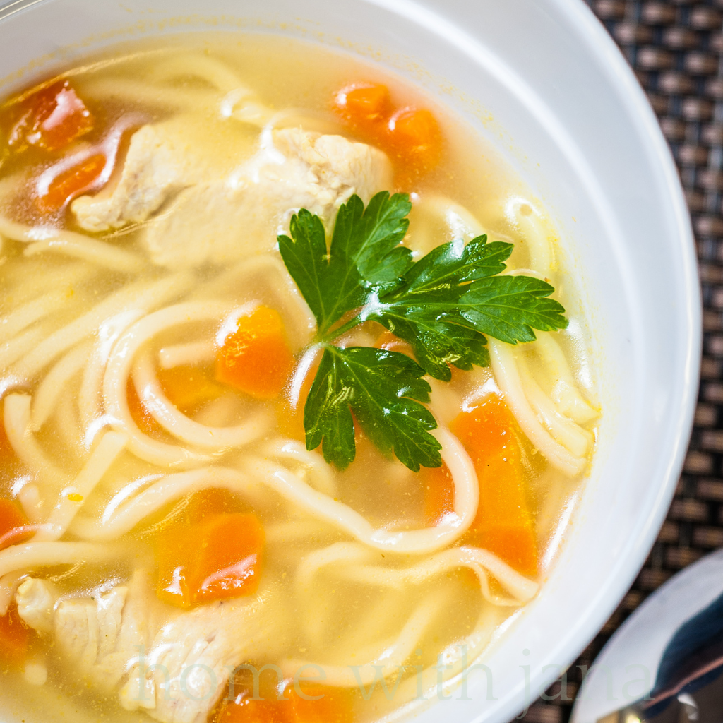 Bowl of homemade chicken noodle soup with carrots, egg noodles, chicken, and fresh parsley garnish