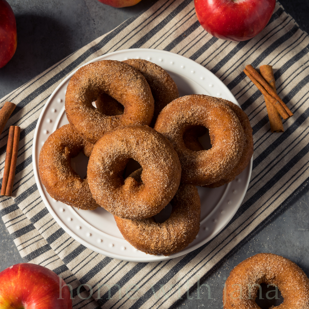 apple cider donuts rolled in cinnamon and sugar placed on a striped placemat.