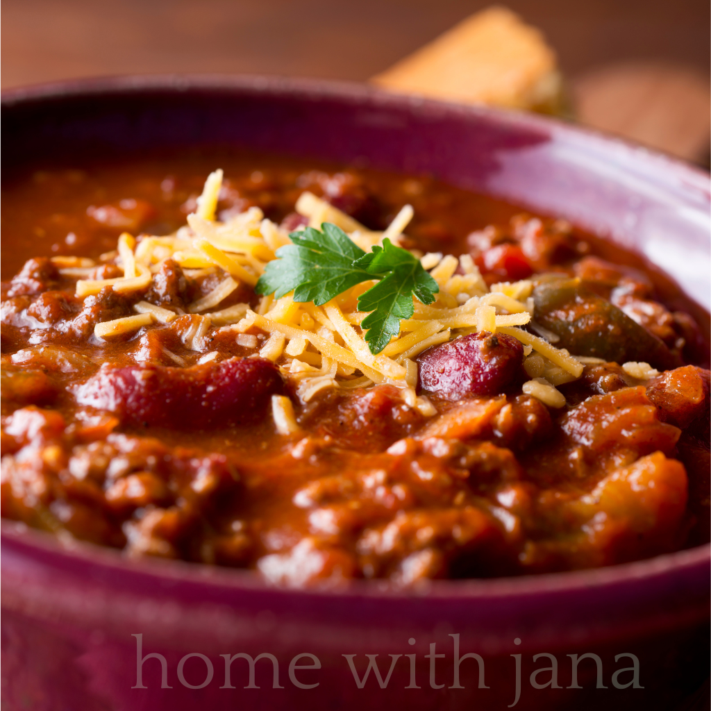 Bowl of homemade beef and bean chili topped with shredded cheddar cheese and fresh parsley