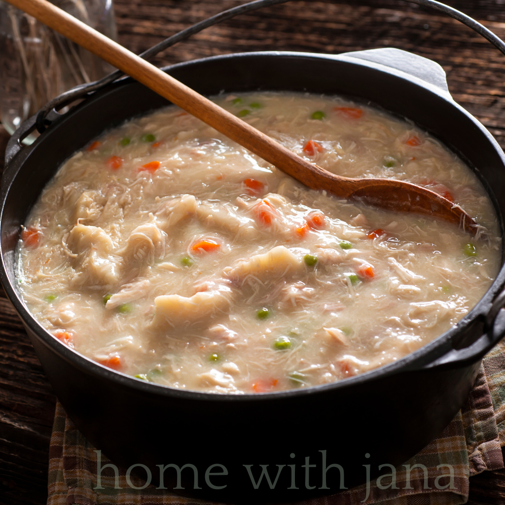 Pot of homemade chicken and dumplings with carrots, peas, and fluffy dumplings in creamy broth