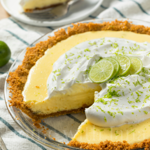 A Key Lime Pie topped with whipped cream and limes in a glass pie pan.