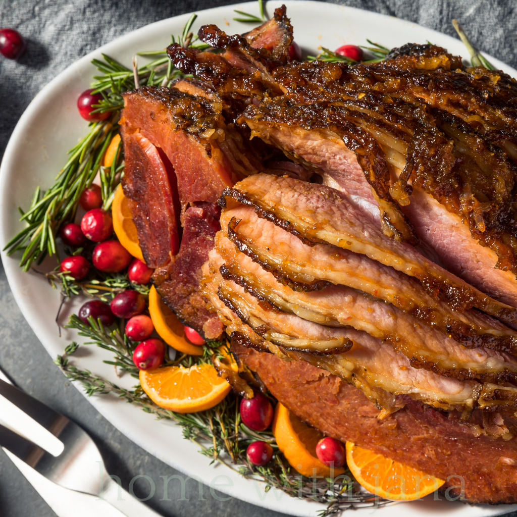 Holiday glazed spiral ham with brown sugar orange glaze, garnished with fresh cranberries, rosemary, and orange slices on a serving platter.