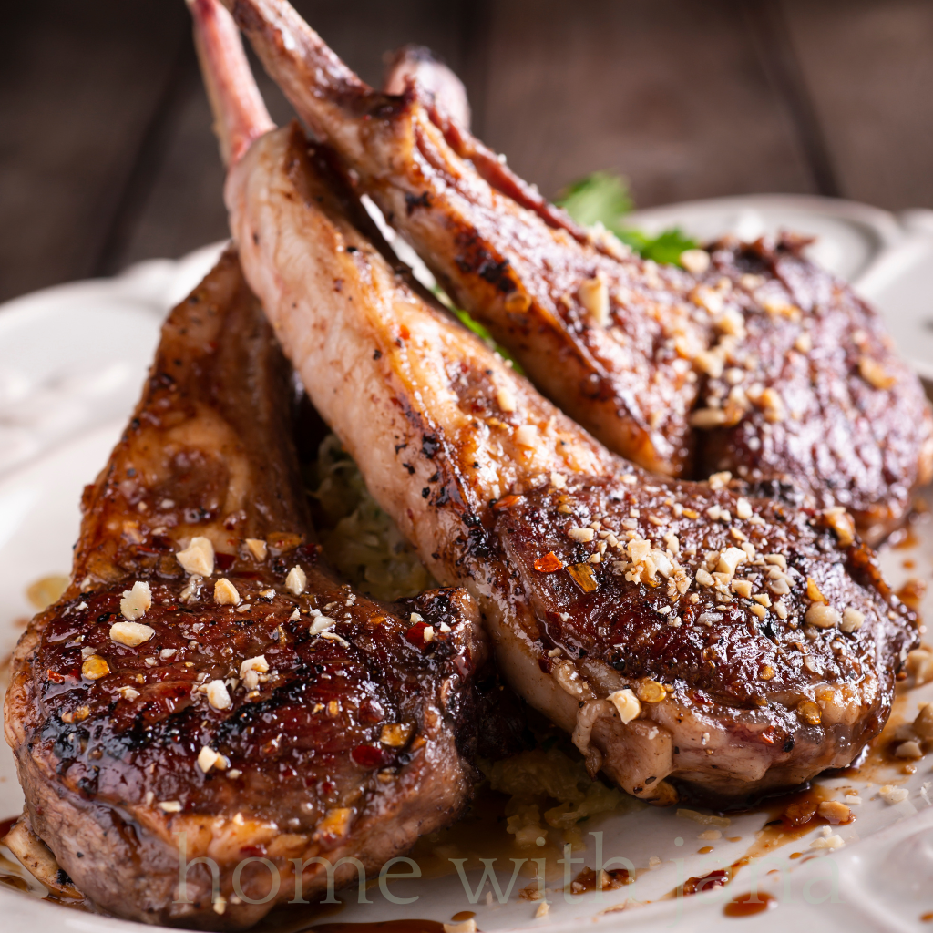 Juicy garlic herb grilled lamb chops with a caramelized crust, garnished with fresh herbs and chopped nuts on a white platter.