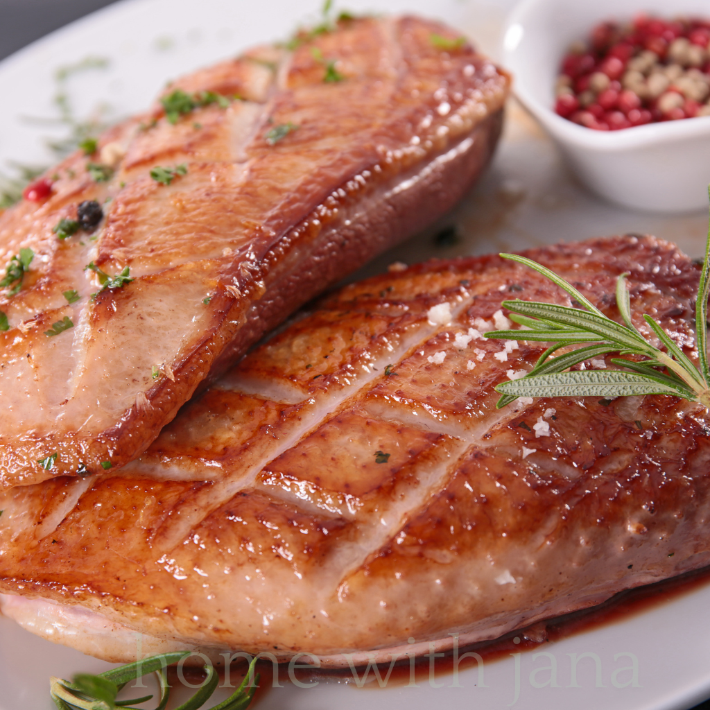 Pan-seared duck breast with crispy golden skin, garnished with rosemary and sea salt on a white plate.