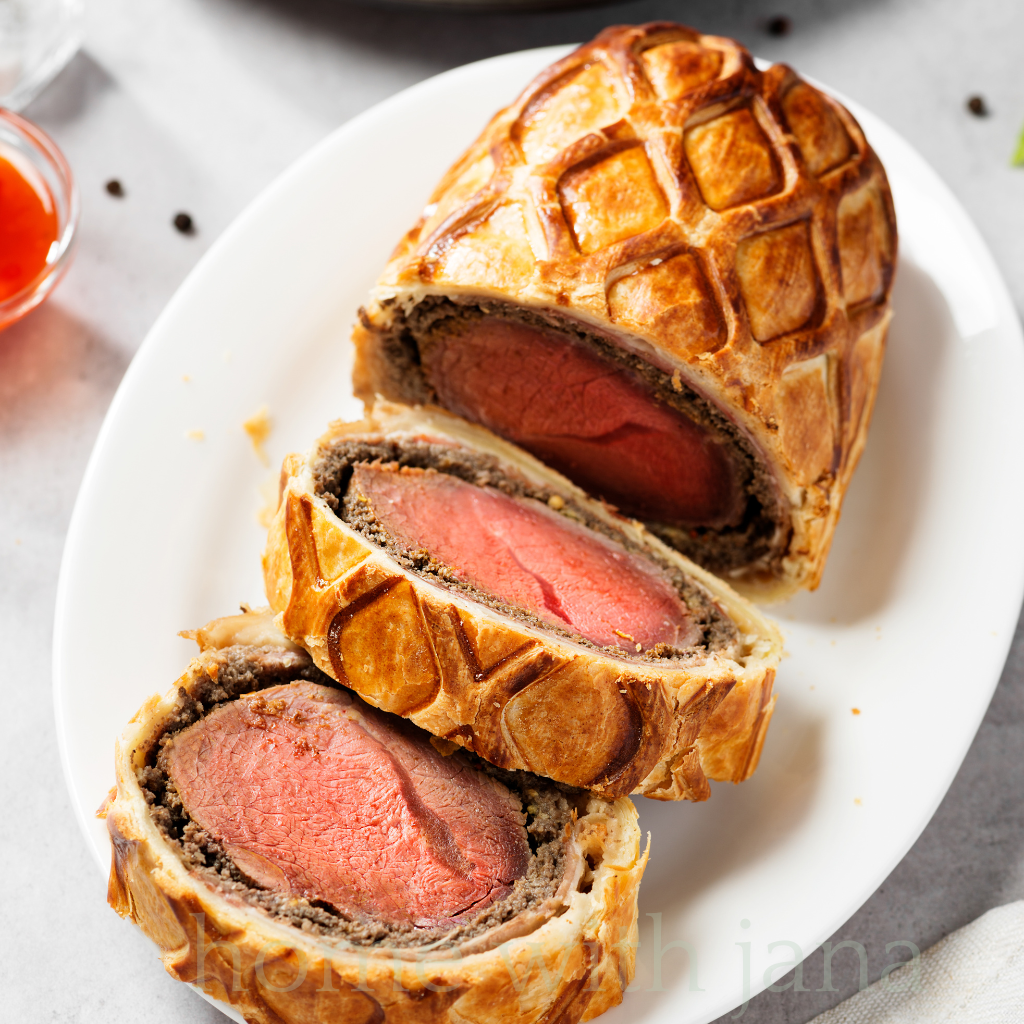 Classic Beef Wellington with golden puff pastry, tender beef tenderloin, and mushroom duxelles filling, sliced and served on a white platter.