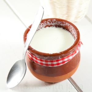 Homemade buttermilk in a rustic clay jar with a spoon, ready for baking and cooking.