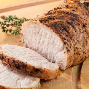 Sliced herb-crusted pork loin roast on a wooden cutting board with fresh thyme.