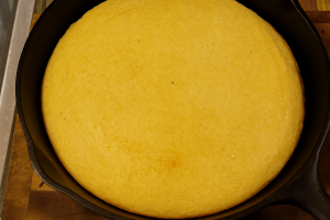 Golden-brown cornbread baked in a cast iron skillet, resting on a wooden surface.