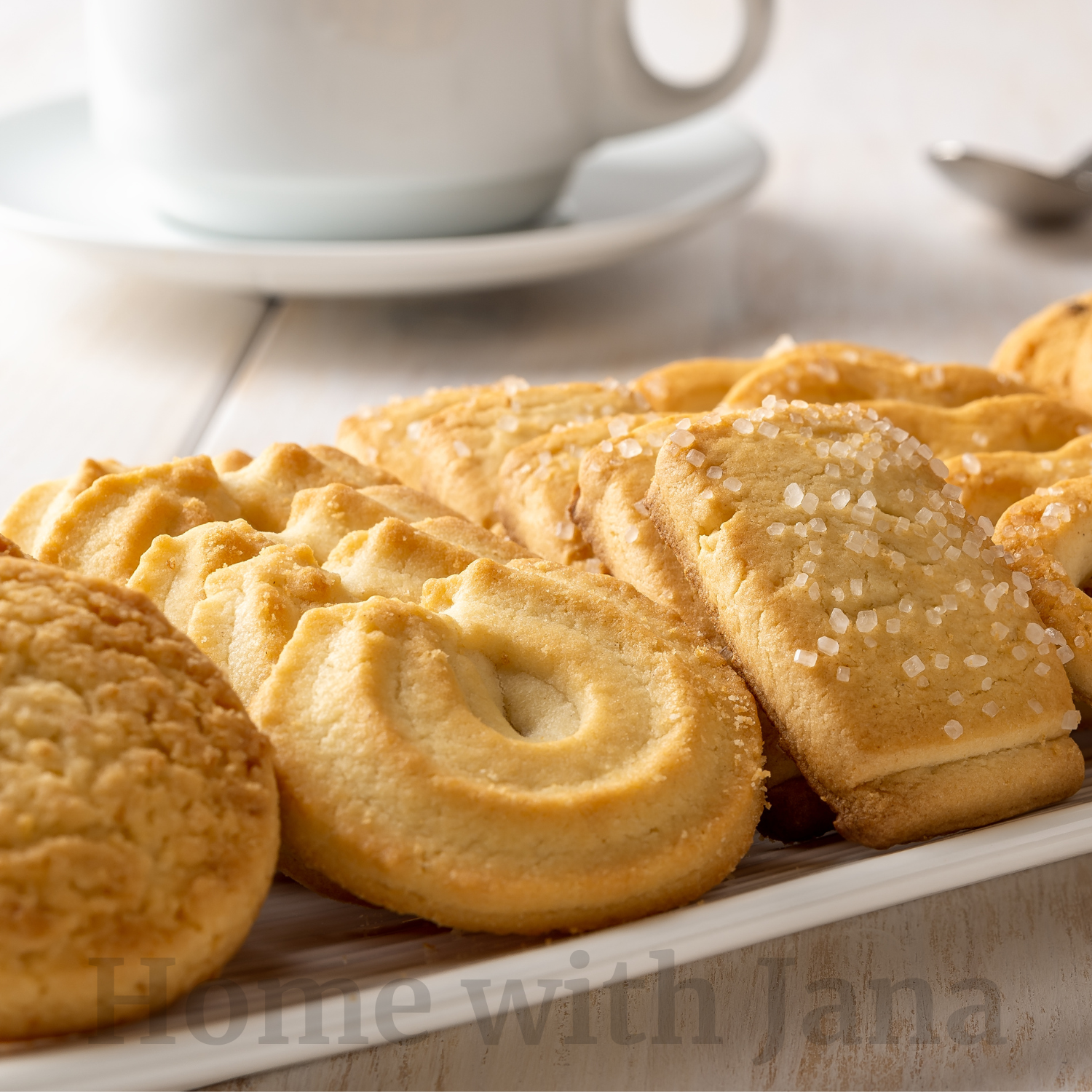 Homemade Danish butter cookies arranged on a white plate, including pretzel shapes, rings, and sugar-topped rectangles.