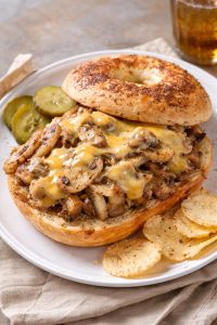Garlic butter bagel sandwich filled with tender pork, sautéed mushrooms and onions, and melted Velveeta cheese