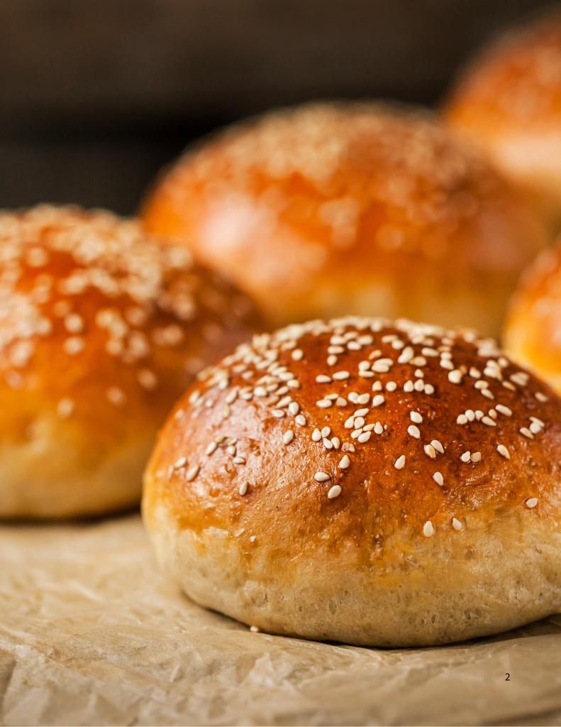 Freshly baked homemade hamburger buns with a golden brown crust and sesame seeds, cooling on parchment paper