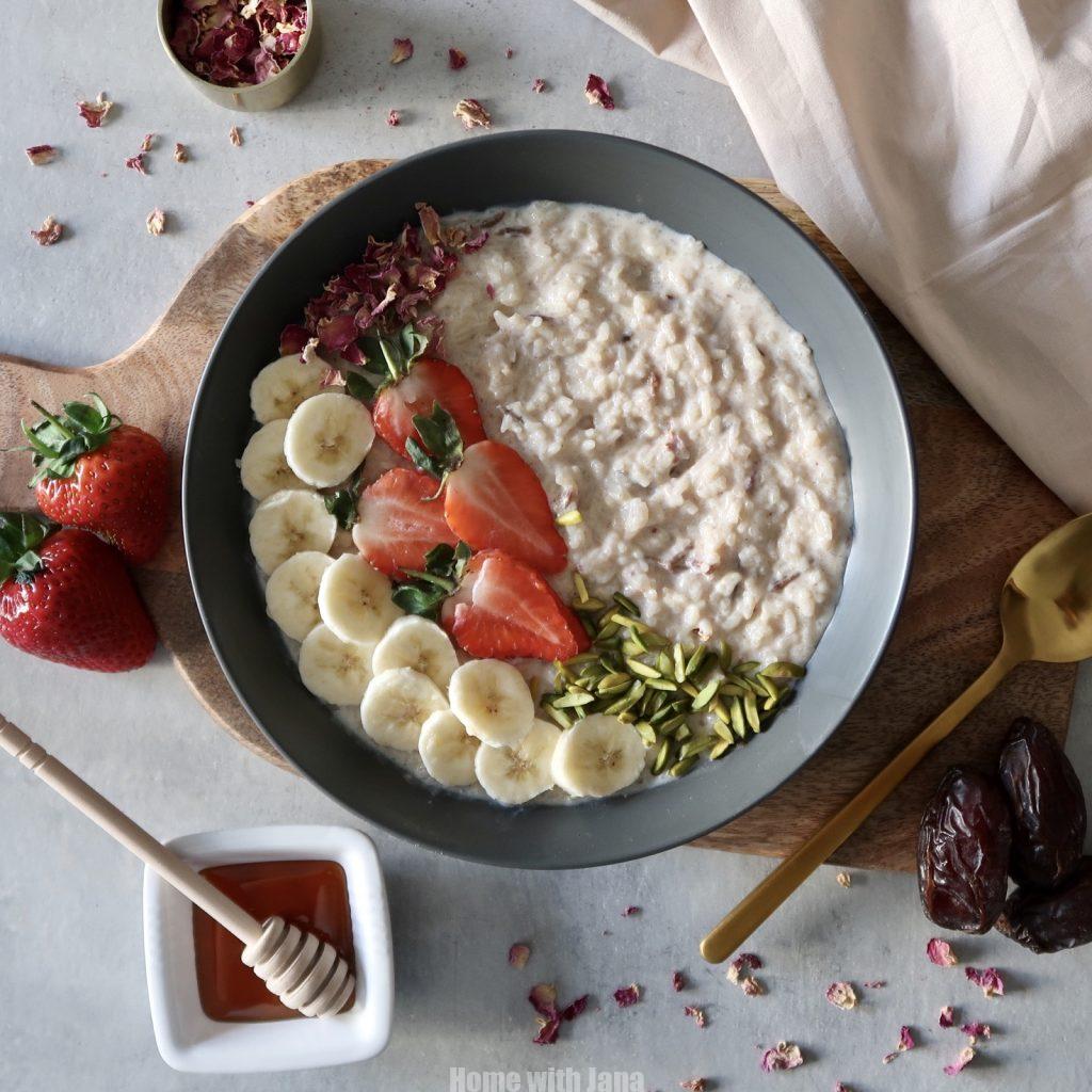 Creamy rice porridge topped with sliced bananas, fresh strawberries, pumpkin seeds, and a drizzle of honey in a gray bowl