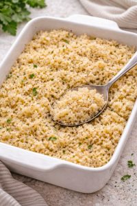 Oven-baked seasoned rice in a white casserole dish with a spoon, fluffy and evenly cooked